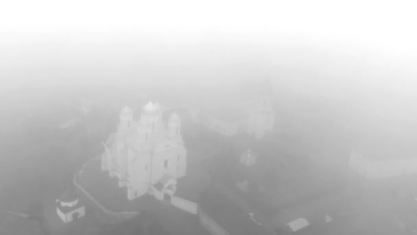 Vuelo matutino en la niebla sobre un monasterio ortodoxo. Video en blanco y negro. Hermosa vista del monasterio de Zimnensky Svyatogorsky desde arriba. Vista de las cúpulas y la Catedral de la Asunción. - Imágenes, Vídeo