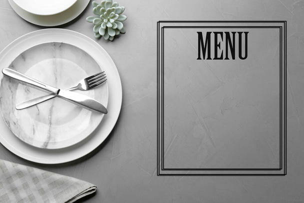 Table setting and empty menu on grey background, flat lay. Space for text - 写真・画像