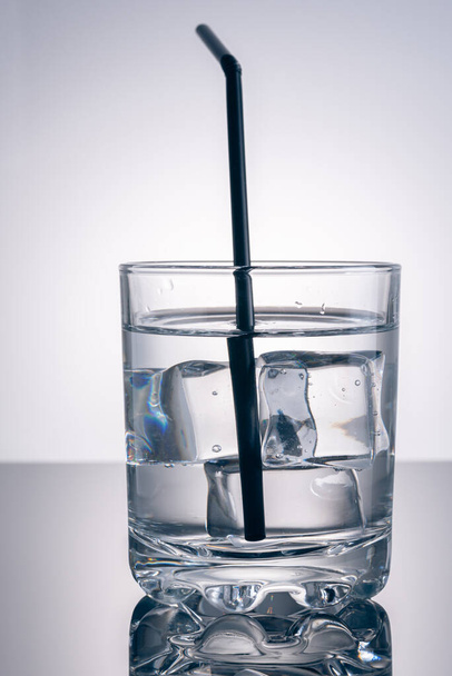 Glas ijs en water met stromend water of plastic rietje - Foto, afbeelding