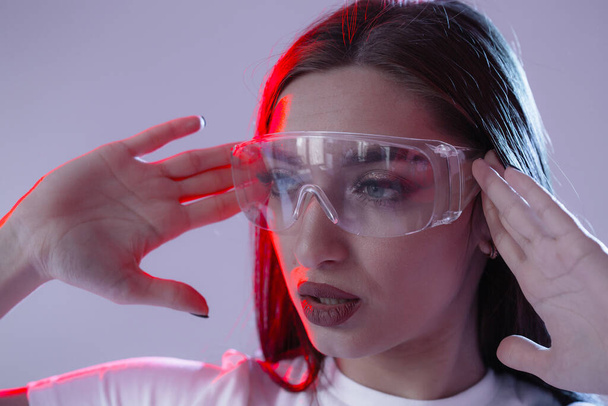 Portrait of young girl holding hands with transparent glasses in neon red light in a studio. Horizontal banner for web sites. - Foto, Imagem
