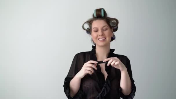 Girl with hair curlers rollers on hair, applying mascara doing makeup. - Imágenes, Vídeo