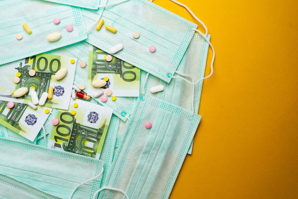 Sale of medical masks. Protective medical mask and different types of pills next to money on yellow background. Coronavirus concept. 2019 nCoV. - Foto, immagini