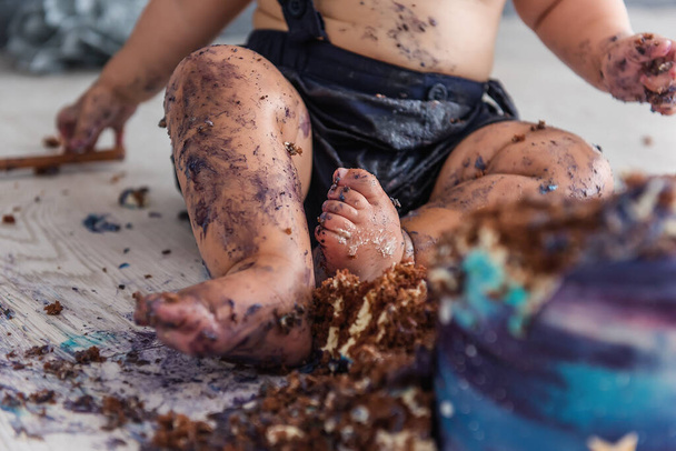 A beautiful little boy ruins his first cake, licks his feet and rolls in blue cream - the first birthday of a babys life, Selective and Back front Focus - Foto, Imagem
