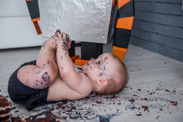 A beautiful little boy ruins his first cake, licks his feet and rolls in blue cream - the first birthday of a babys life, Selective and Back front Focus - 写真・画像