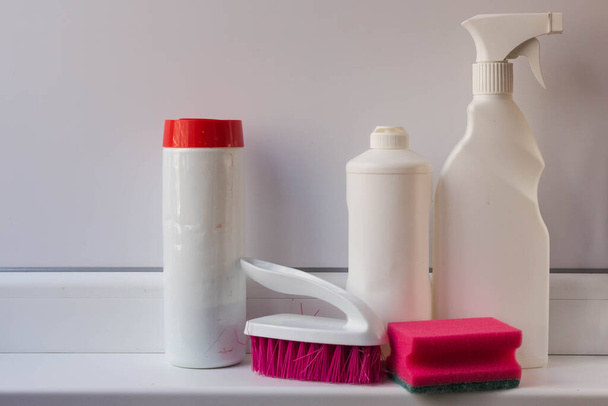 Eszközök a ház takarításához. Tisztító gél, por és spray tisztítására és fertőtlenítésére különböző felületek műanyag fehér tartályokban rózsaszín kefével és szivacs fehér alapon. - Fotó, kép