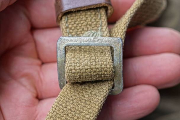 vingers houden een grijze metalen karabijn op een oud groen harnas gemaakt van stof op een rugzak - Foto, afbeelding