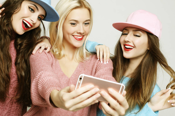 Three happy best girlfriends wearing sweaters and caps making selfie - Valokuva, kuva