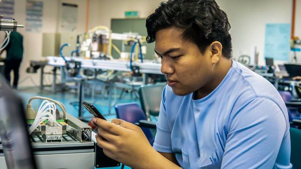 Nuori malaijilainen insinööri, joka työskentelee laboratoriossa älypuhelimella, jossa on automaatiokonejärjestelmä. Kuva sisältää melun vähentämistä. Valittu painopiste
. - Valokuva, kuva