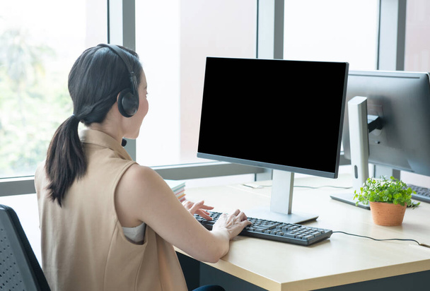 Rare view of attractive and smile young asian customer servicer woman wearing headset in modern creative meeting working office look at computer monitor,work from and social distancing concept. - Zdjęcie, obraz