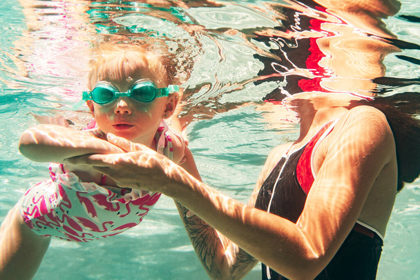 young mother with little girl in swimming swimsuits swimming underwater in the pool  - Fotografie, Obrázek