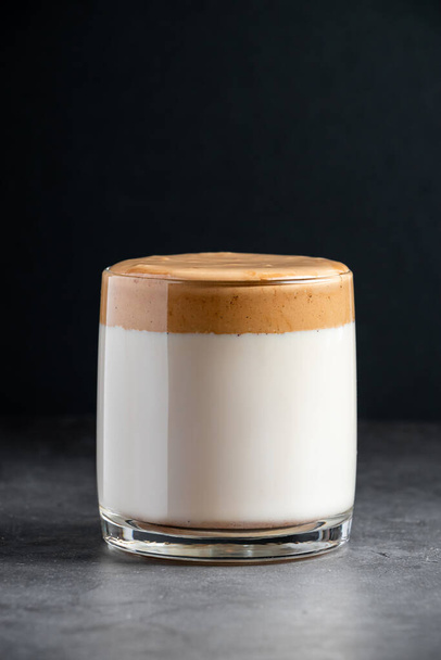 Dalgona coffee on a dark background. A glass of trendy Korean ice drink made from milk and fluffy foam. Vertical photo - Photo, image