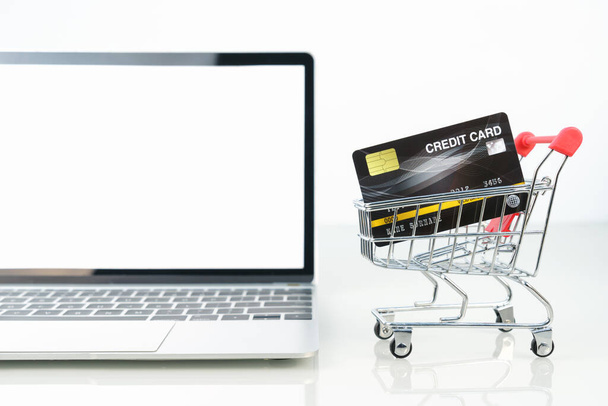 Cartão de crédito no carrinho de compras frente da tela em branco do laptop para compras on-line no branco, trabalho do conceito home
 - Foto, Imagem