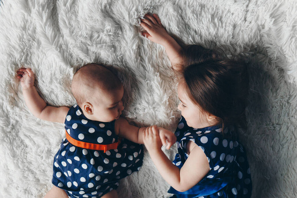the concept of a healthy lifestyle, the protection of children, shopping - a teenager with a newborn baby playing together. Happy kids: sisters lying on the floor on white background. the view from the top - Foto, immagini