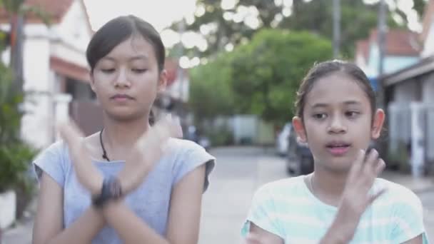 Schattig Aziatisch meisje en haar zus genieten ervan om heerlijk te dansen tijdens het staan op het pad in een woonwijk. Activiteiten van vrouwelijke tieners tijdens vakanties in de woonwijk. - Video