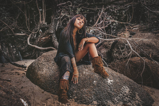 beautiful young stylish tribal style woman sitting on the rock outdoors - Fotoğraf, Görsel