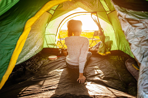 The woman asian who just woke up inside the tent was watching the sunrise in the morning as a holiday activity in the forest path autumn season. Hiking, hiker, alone, forest, camping, activity concept. - Φωτογραφία, εικόνα