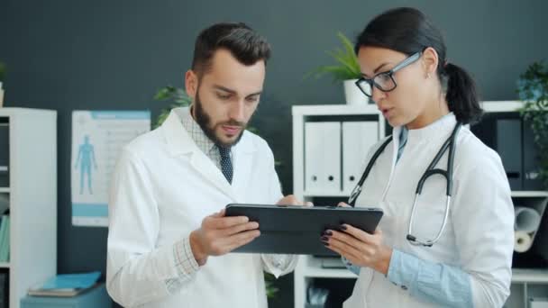 Lääkintämiehet valkoisissa kaavuissa käyttävät tablettia töissä puhumalla käyttäen gadget toimistossa
 - Materiaali, video