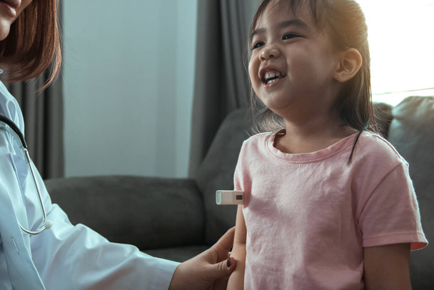 Asiática médico femenino está utilizando un termómetro para medir la fiebre de los niños en su casa
. - Foto, imagen