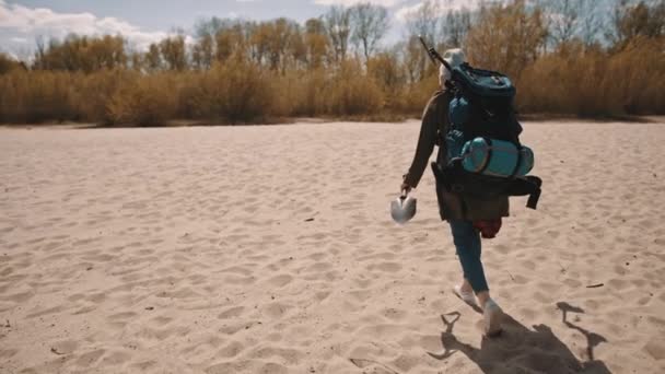 Explorer με το σακίδιο πλάτης, το παπούτσι και τον μεταλλικό ανιχνευτή περπατώντας στην αμμώδη παραλία. ψάχνοντας για το θησαυρό - Πλάνα, βίντεο