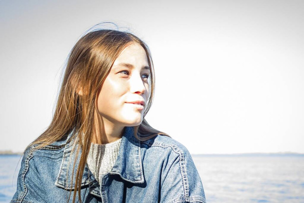 Modern youth fashion, denim, casual style. Portrait of a young girl in a blue denim jacket. Away seascape. Vignetting, copy space. - Photo, Image