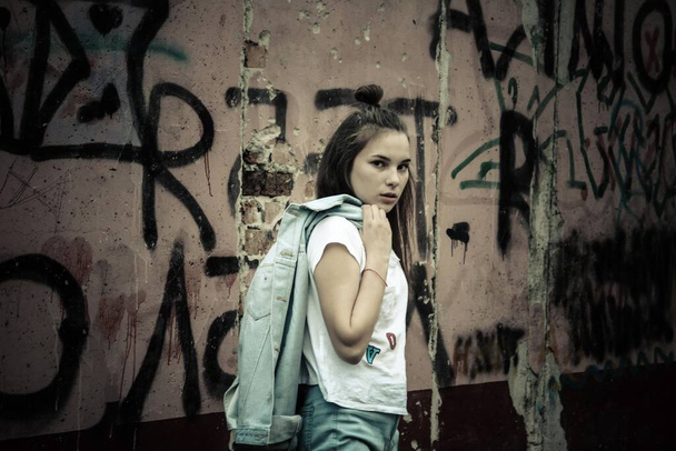 Uma rapariga moderna no fundo de uma parede em ruínas. Aos olhos do desafio, protesto, insolência, desobediência. Adulto, idade de transição. Iluminação diurna, vinheta
. - Foto, Imagem