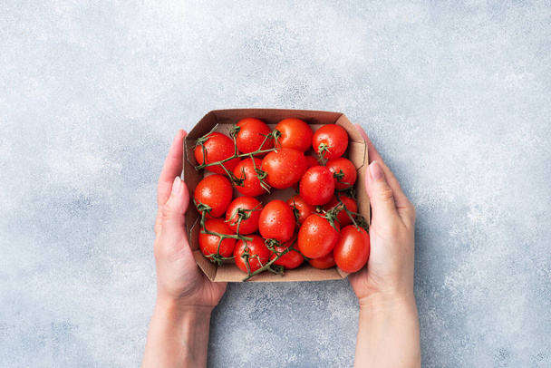 Ripe fresh cherry tomatoes on a branch in a cardboard package Women's hands hold a paper package with tomatoes. - Foto, imagen