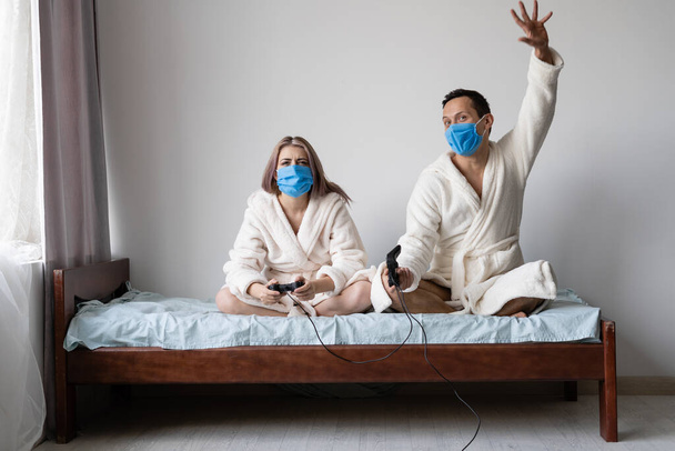 husband and wife are sitting at home on the bed playing games. Joysticks are held in hands. The man is a winner. Place for text - Fotografie, Obrázek