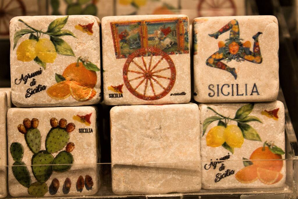 gekleurde afbeeldingen weergegeven op kubusvormige stenen ter promotie van de regio Sicilië in Italië met citrusvruchten, citroenen, sinaasappels, cactussen typische Siciliaanse kar en vrouwelijke kop met drie gevouwen benen genaamd "Trinacria" symbool van de regio Sicilië - Foto, afbeelding
