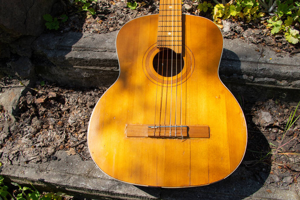 Дерев "яна коричнева гітара лежить на кам" яній дорозі на вулиці у весняній траві в Україні. - Фото, зображення