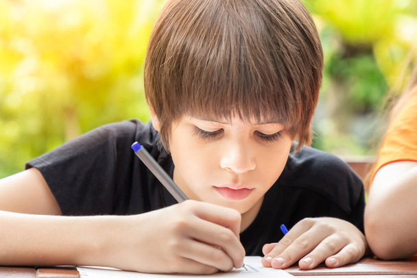 Porträt eines süßen Jungen, der zeichnet und zu Hause Hausaufgaben im Garten macht - Foto, Bild
