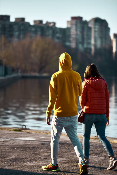 Egy sárga kabátos fickó és egy piros kabátos lány sétálnak a kikötőben a víz mellett, és elöl néznek. Csend, béke és természet. létra a vízhez. utcai fotó. elegánsak.. - Fotó, kép