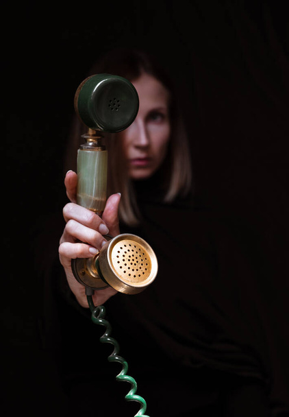 Jeune, belle femme floue tenant un téléphone rétro vintage isolé sur fond noir
. - Photo, image