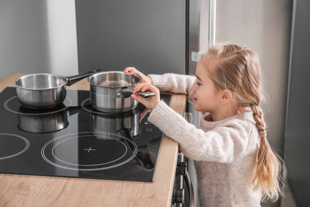 Kleines Mädchen spielt zu Hause mit Kochtopf auf Elektroherd - Foto, Bild
