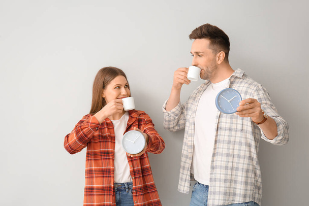 Young couple with coffee and alarm clocks on light background - Photo, image