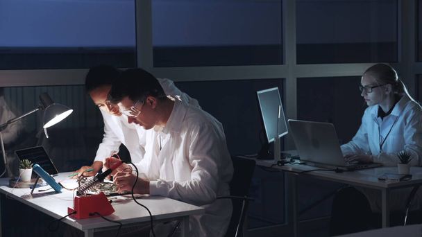 Мультирасовые мужчины и женщины проверяют материнскую плату с помощью тестера мультиметра в лаборатории электроники
 - Фото, изображение