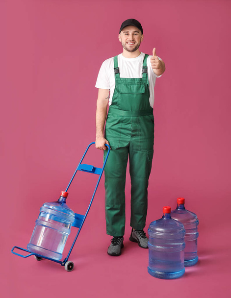 Delivery man with bottles of water on color background - Photo, image