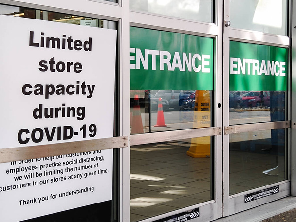 As portas de entrada deslizantes de um grande supermercado estão fechadas e mostrando um sinal sobre a capacidade limitada durante a pandemia de Covid-19
. - Foto, Imagem