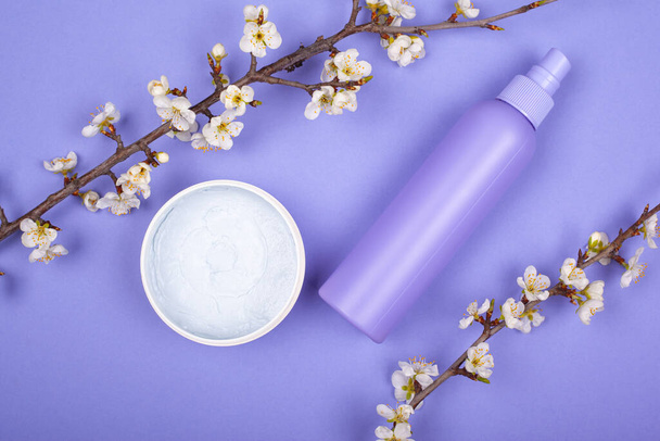 Creme-Kosmetik und blühende Zweige auf violettem Hintergrund. Hautpflegekonzept, Schönheit - Foto, Bild