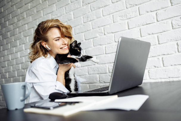 Smiling woman with black cat in her arms sitting at table with laptop. - Photo, Image