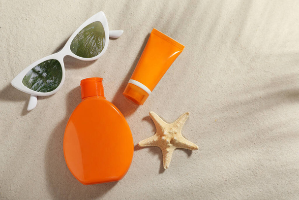 Sunglasses with reflection of palm trees and protection cosmetic products on sand, flat lay. Space for text - Photo, Image