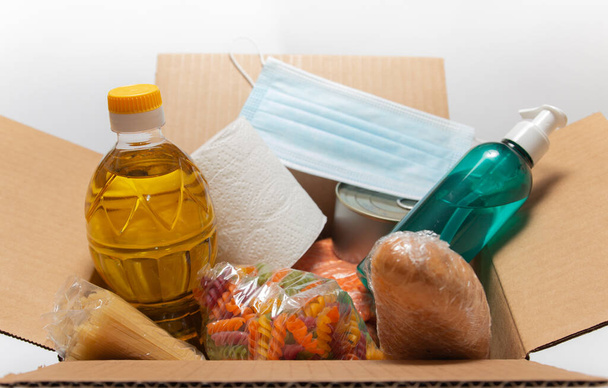 Donation goods in carton box on the white background. Pasta, toilet paper, medical mask, sunflower oil, sanitizer, caned food, bread. Food delivery for those who need. - 写真・画像