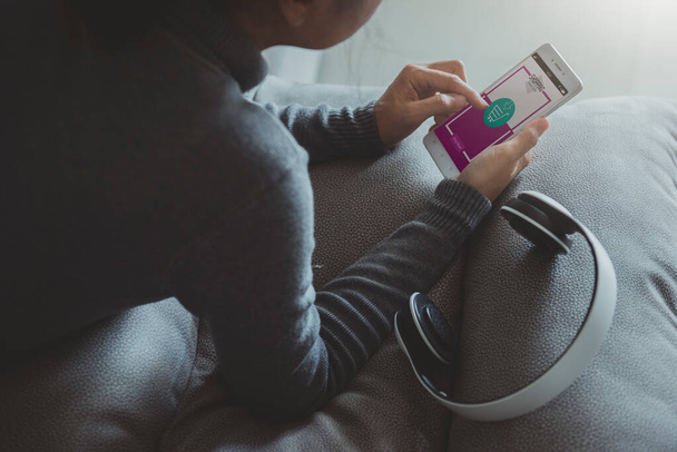Junge Frau kauft mit Smartphone online ein, während sie zu Hause im Wohnzimmer auf dem Sofa liegt. Online-Shopping und modernes Lifestylekonzept - Foto, Bild