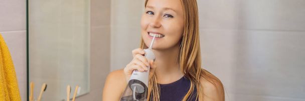 Woman using an oral irrigator in bathroom BANNER, LONG FORMAT - Photo, Image