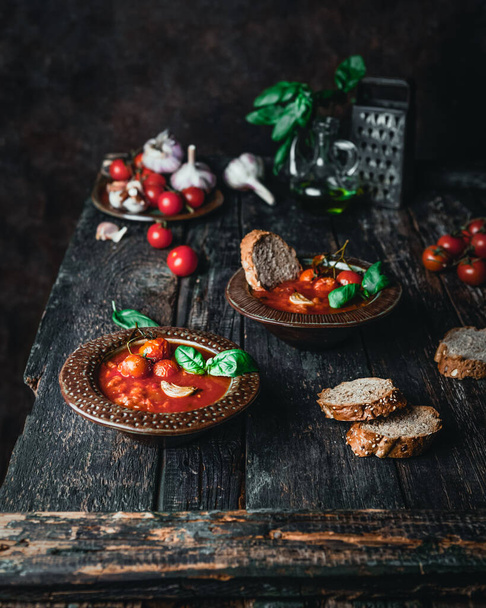 bowls with tomato soup and basil leaves and bred slices with vegetables and grater on wooden table, top view  - Photo, image