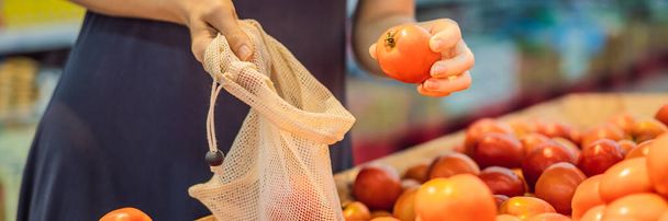 A woman chooses tomatoes in a supermarket without using a plastic bag. Reusable bag for buying vegetables. Zero waste concept BANNER, LONG FORMAT - Photo, Image