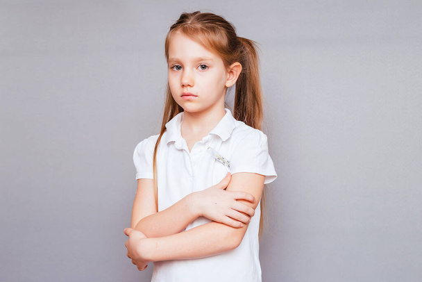 Little girl on a gray background in a white T-shirt measures the temperature - Photo, Image