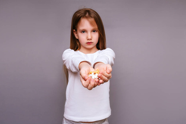 Κορίτσι με μακριά μαλλιά σε γκρι φόντο σε λευκό σακάκι κρατά ένα δισκίο στα χέρια του - Φωτογραφία, εικόνα