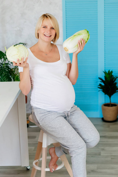 Bionda incinta in cucina a tavola analizza il cavolo verde
 - Foto, immagini