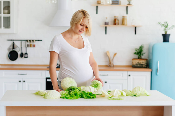 Bionda incinta in cucina a tavola analizza il cavolo verde
 - Foto, immagini