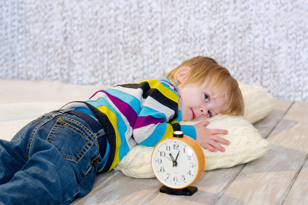 Tired toddler lying down with alarm clock in front - Zdjęcie, obraz